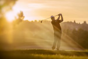 Mid adult golfer teeing of at sunset.